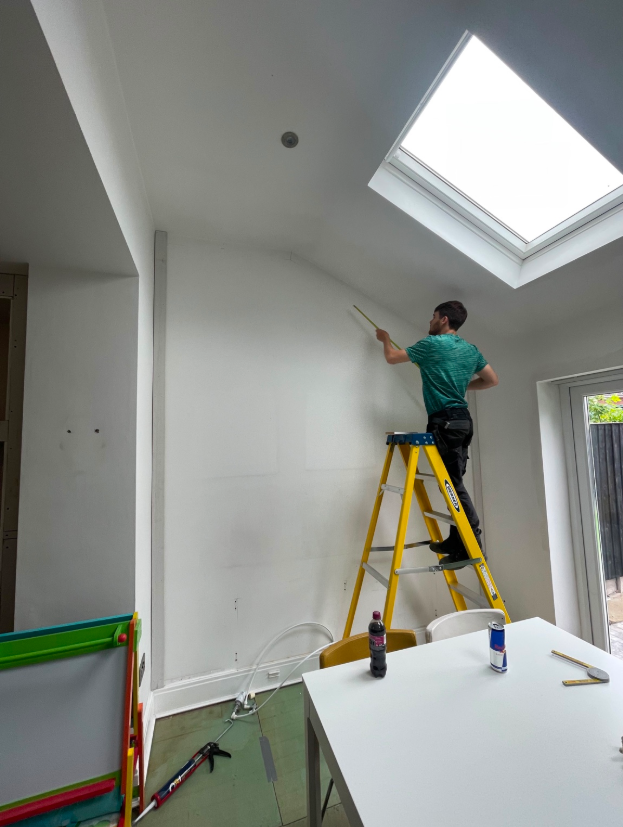 Joiner measuring and preparing an interior wall beneath a rooflight.